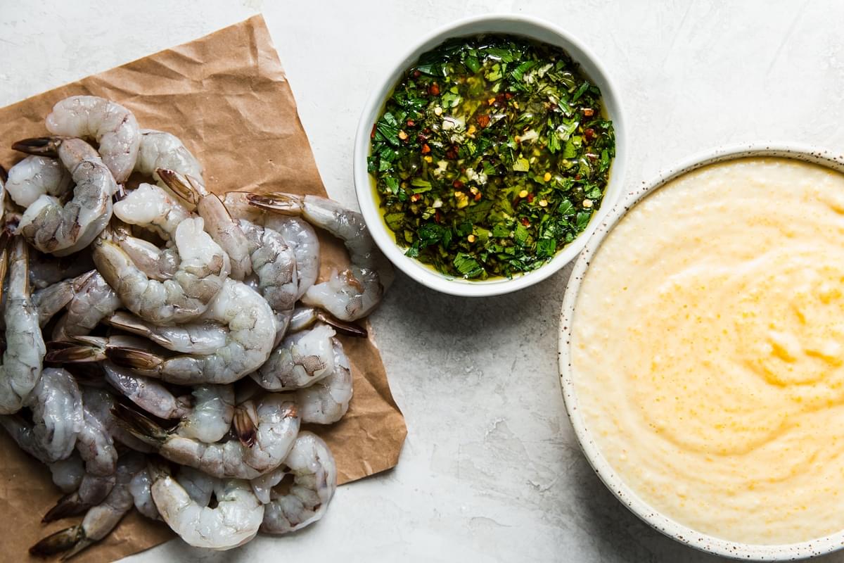 raw shrimp on parchment, chimichurri and polenta in a bowl
