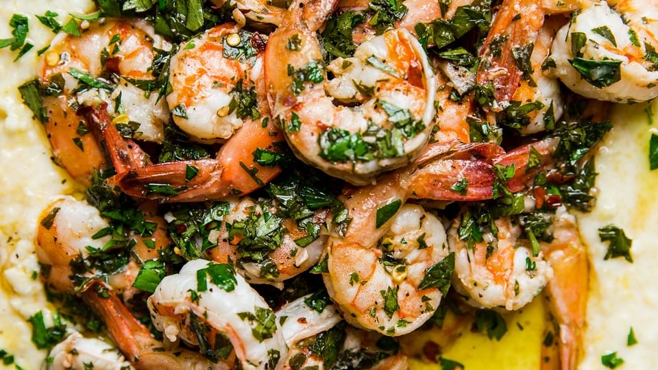 A plate with creamy polenta and chimichurri marinated shrimp with a serving spoon