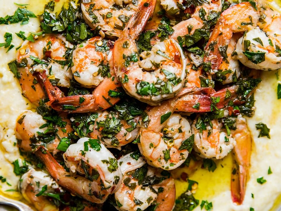 A plate with creamy polenta and chimichurri marinated shrimp with a serving spoon