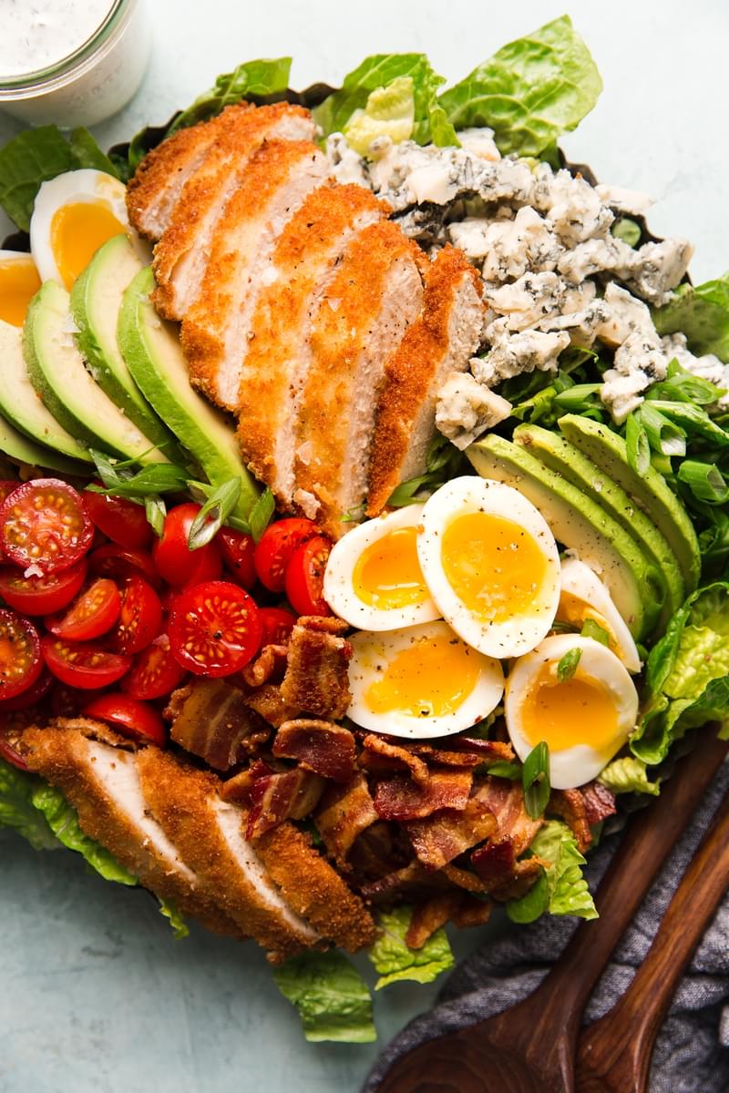 cobb salad with crispy panko chicken, buttermilk ranch dressing, avocados, bacon, soft boiled eggs, blue cheese and tomatoes