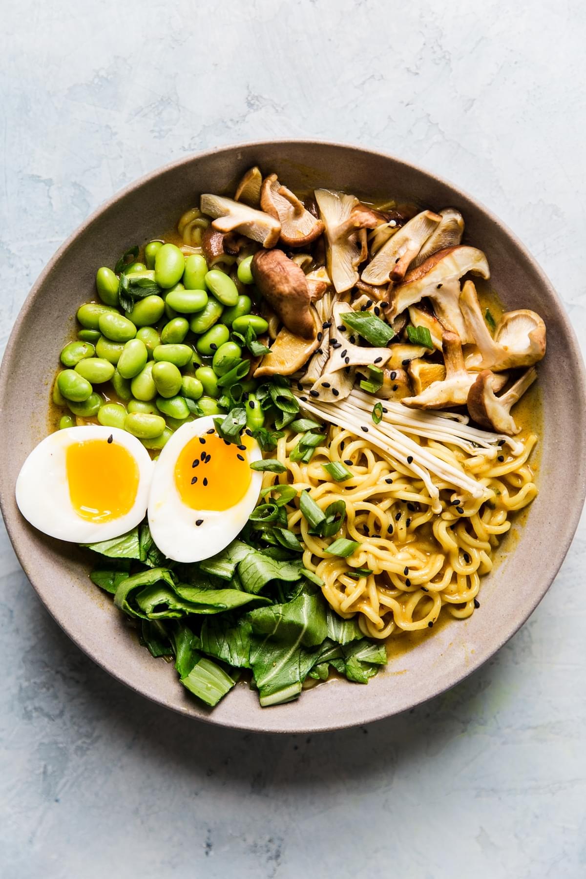Bowl of vegetarian coconut curry ramen with mushrooms, bok choy, edamame and soft boiled egg