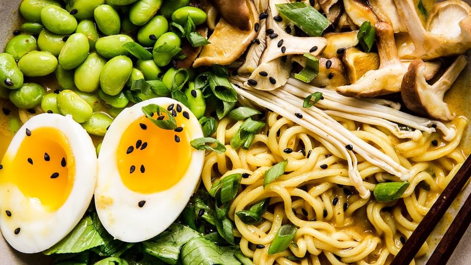 Bowl of vegetarian coconut curry ramen with mushrooms, bok choy, edamame and soft boiled egg with chopsticks