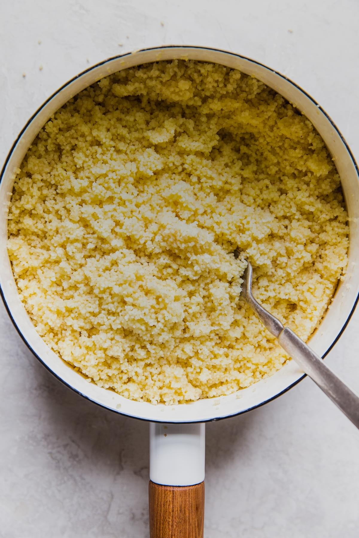 white soup pot filled with couscous being fluffed with a fork