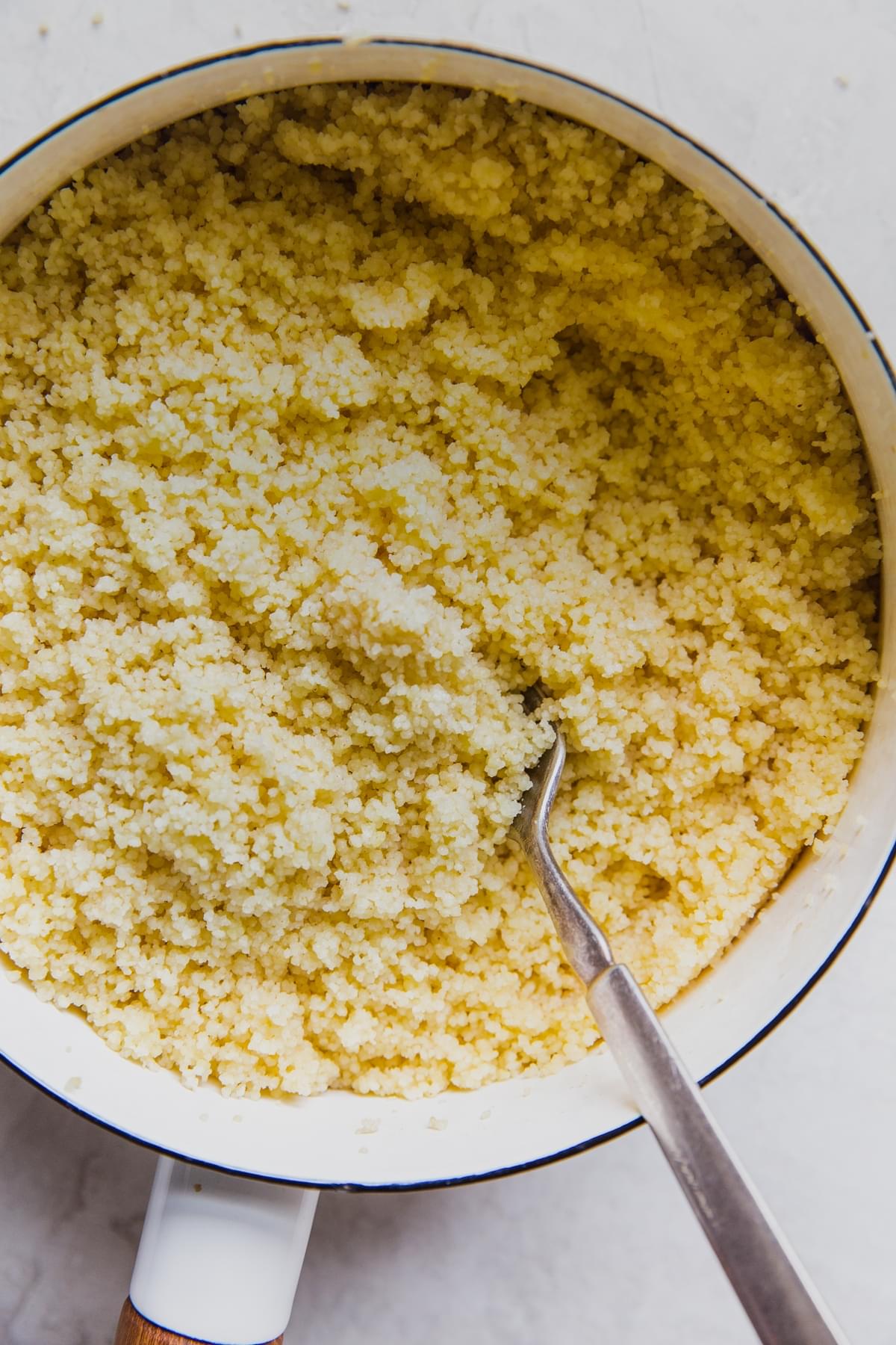 white soup pot filled with couscous being fluffed with a fork