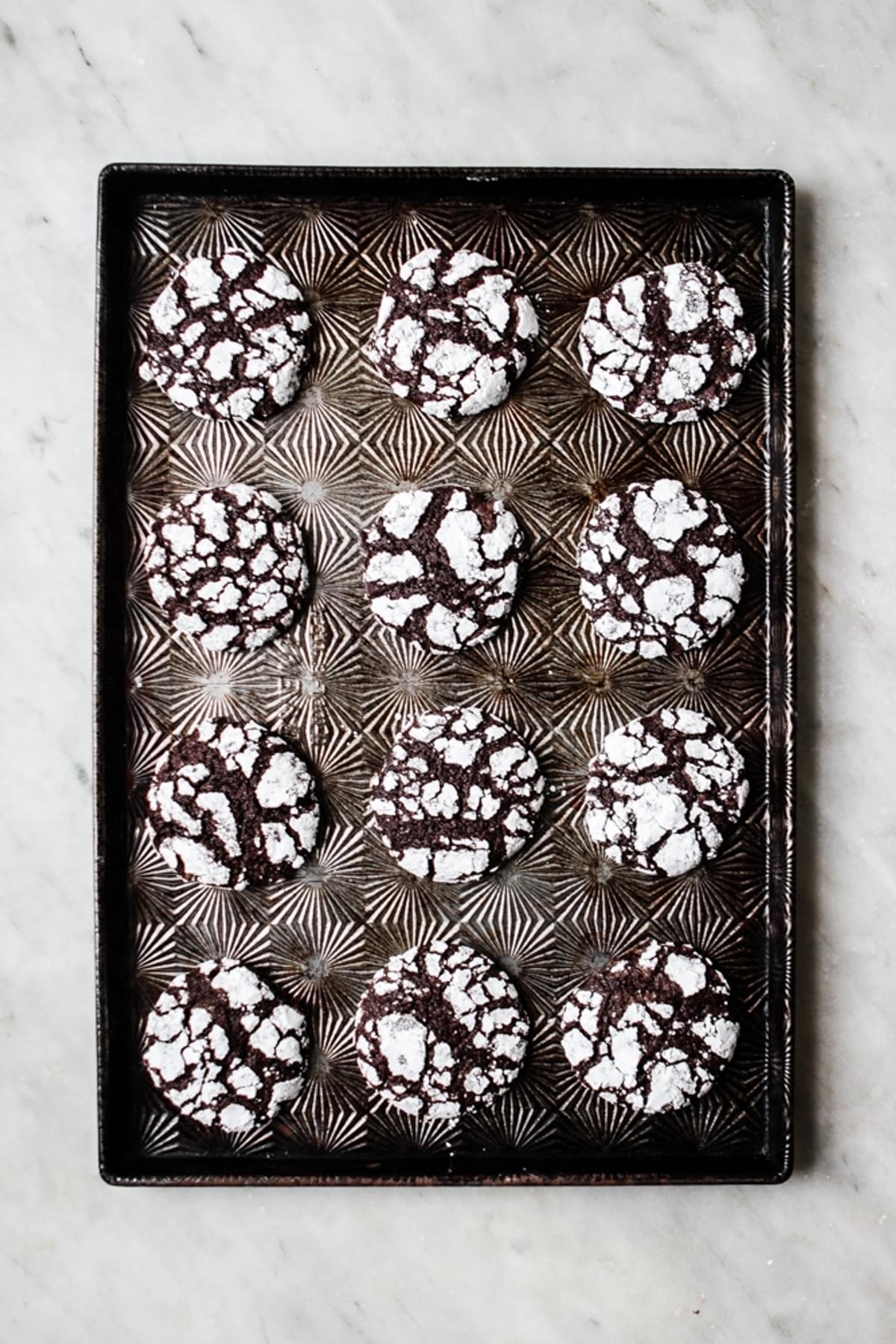 chocolate crinkle cookies rolled in powdered sugar baked on a cookie sheet