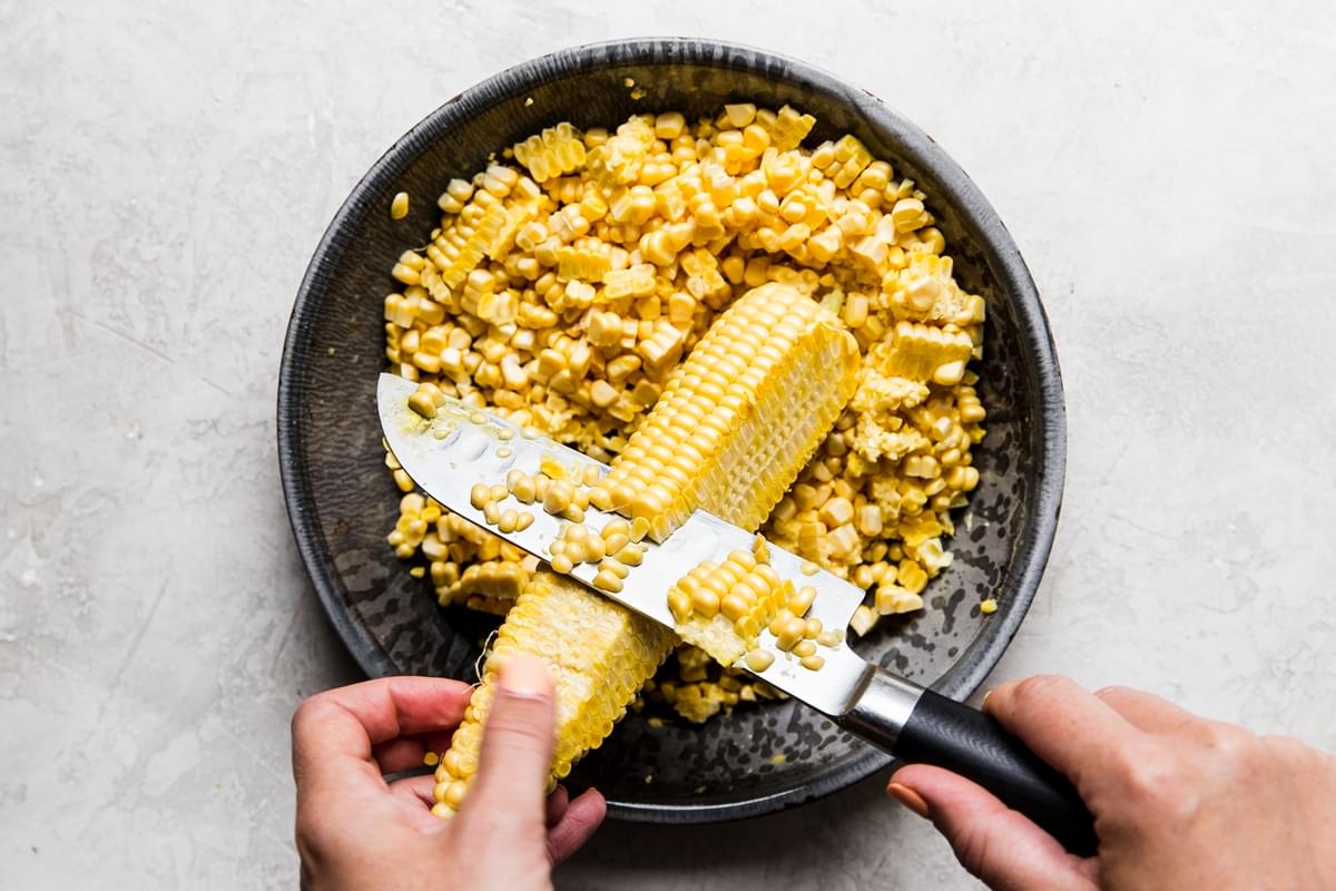 knife removing corn kernels from corn over a pie pan