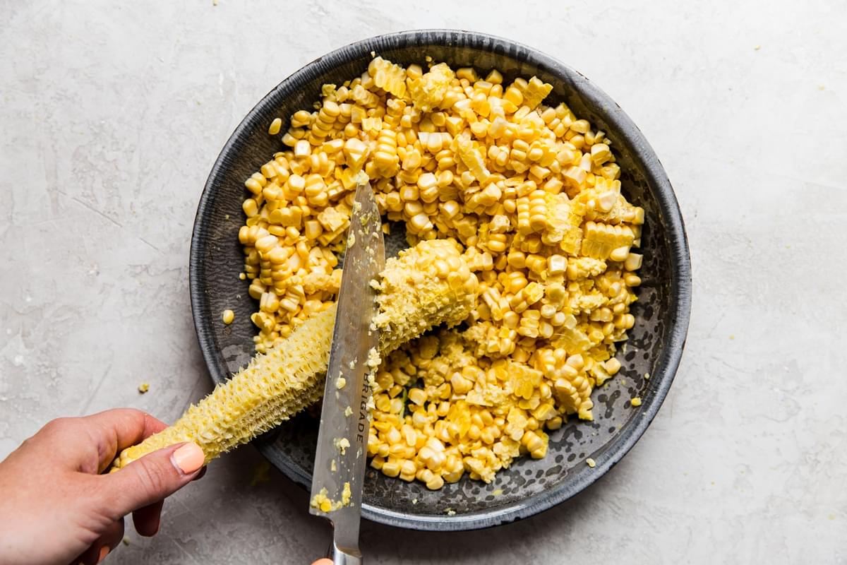 back of knife removing corn kernel liquid from corn over a pie pan