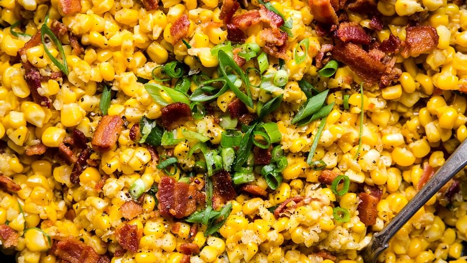 A cast iron skillet filled with dairy free creamed corn with bacon and green onions