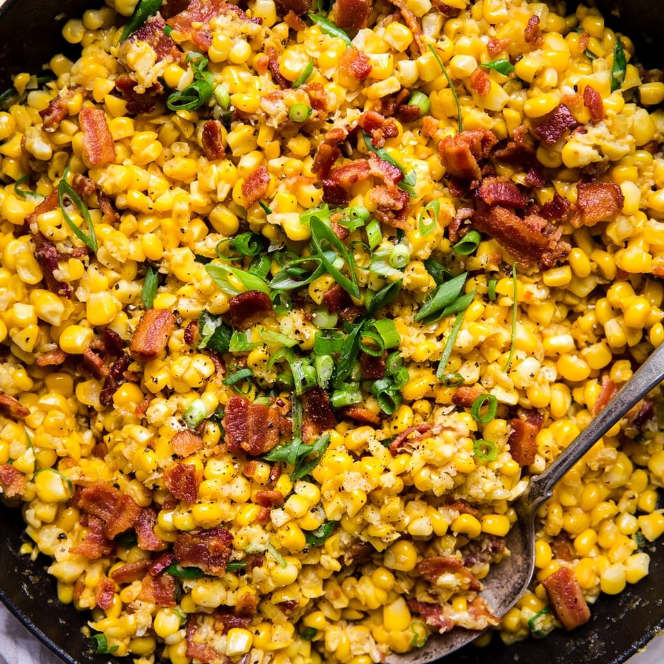 cast iron skillet filled with dairy free creamed corn with bacon and green onions