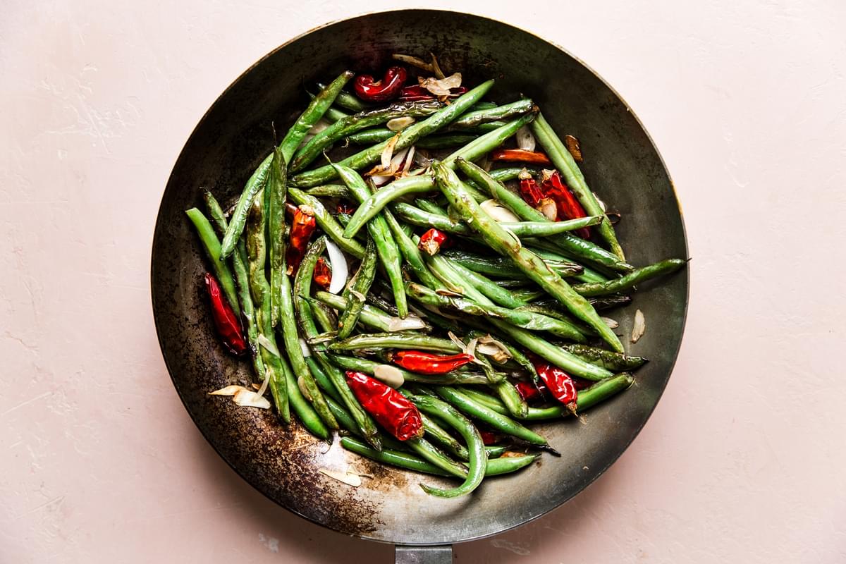 dry fried green beans in a skillet with raw garlic slices and dried red chillies