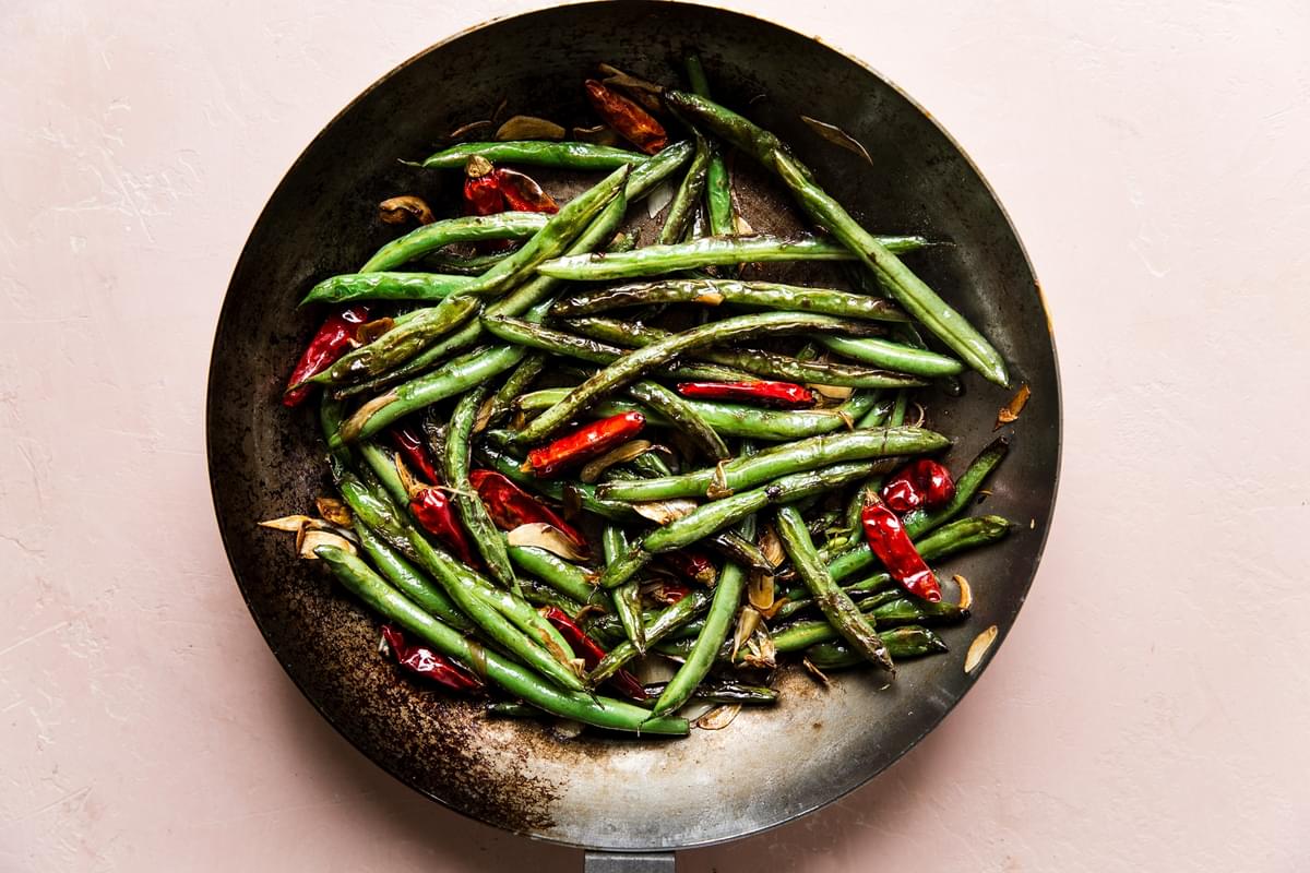 dry fried green beans with dried red chillies and garlic in a skillet with sauce