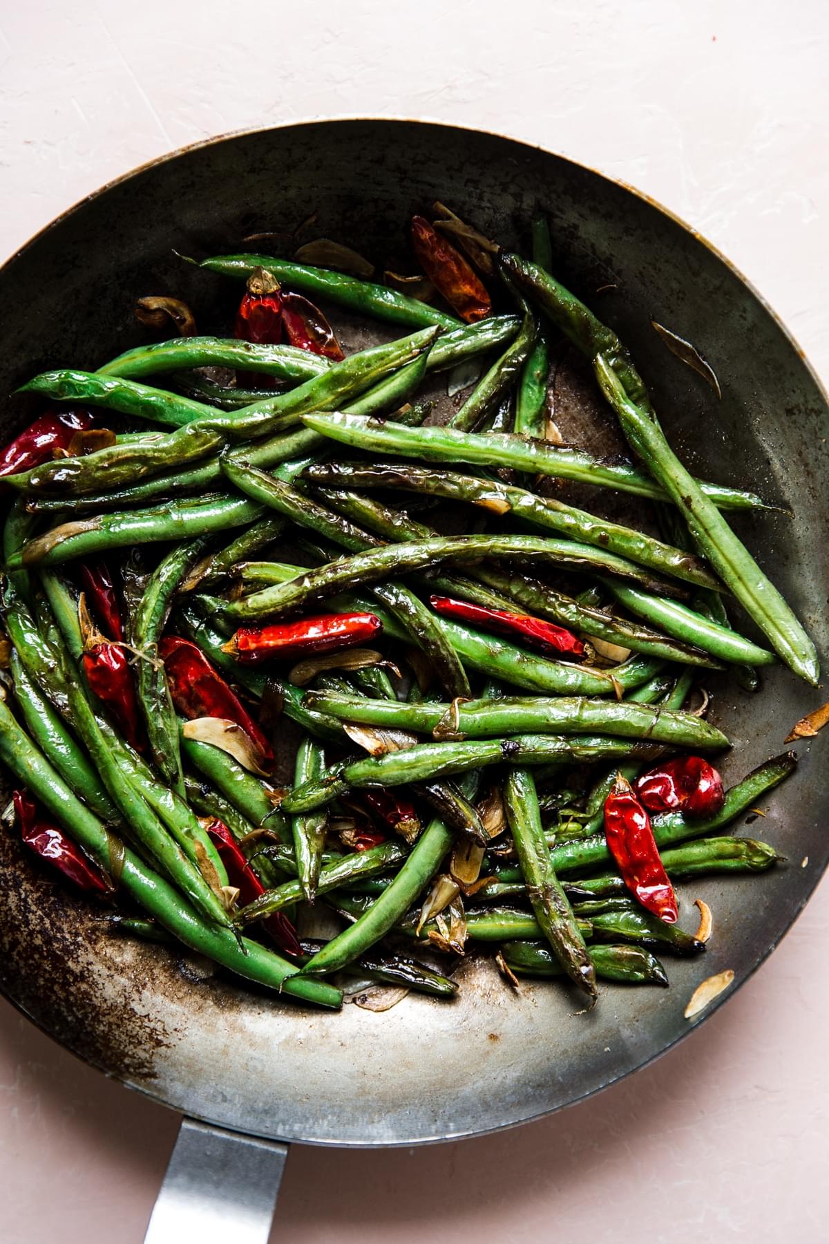 dry fried green beans in a skillet with dried chillies and sliced garlic cloves