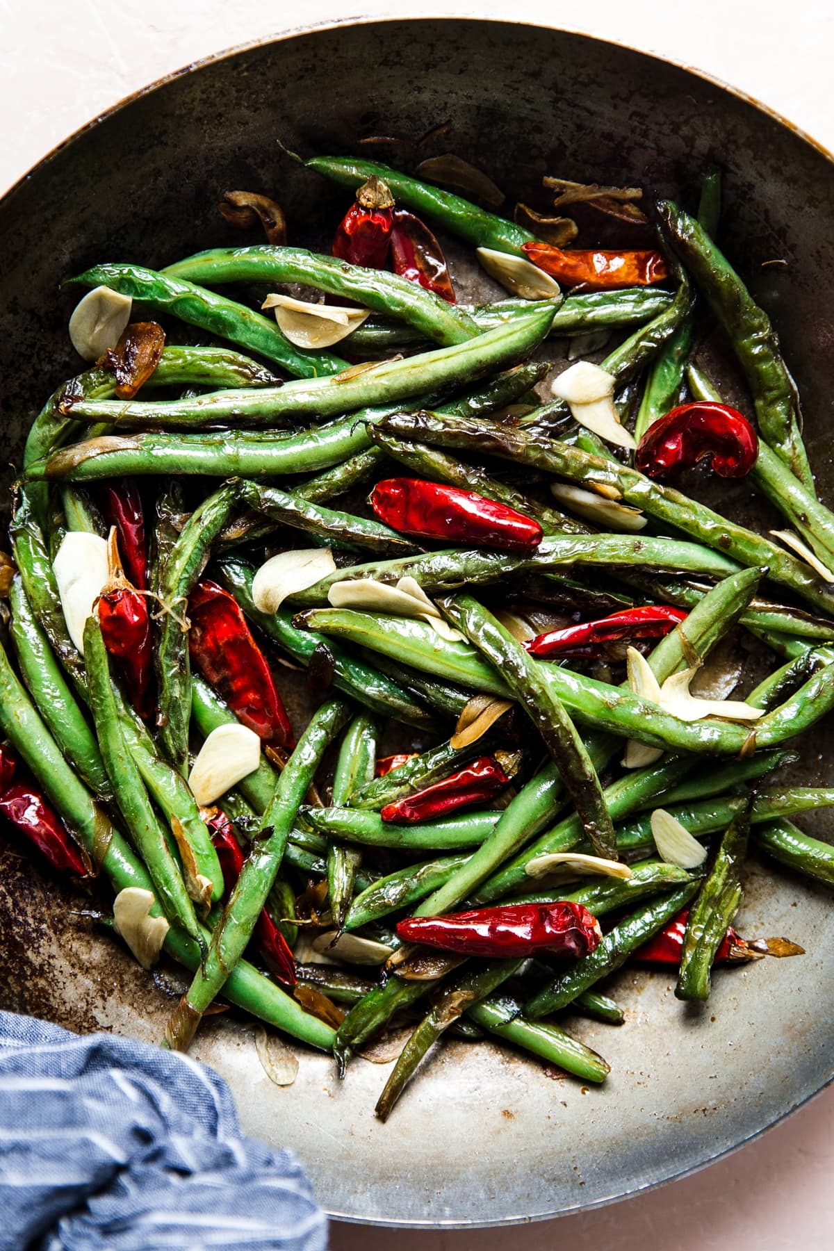 dry fried green beans in a skillet with red chillies and garlic cloves