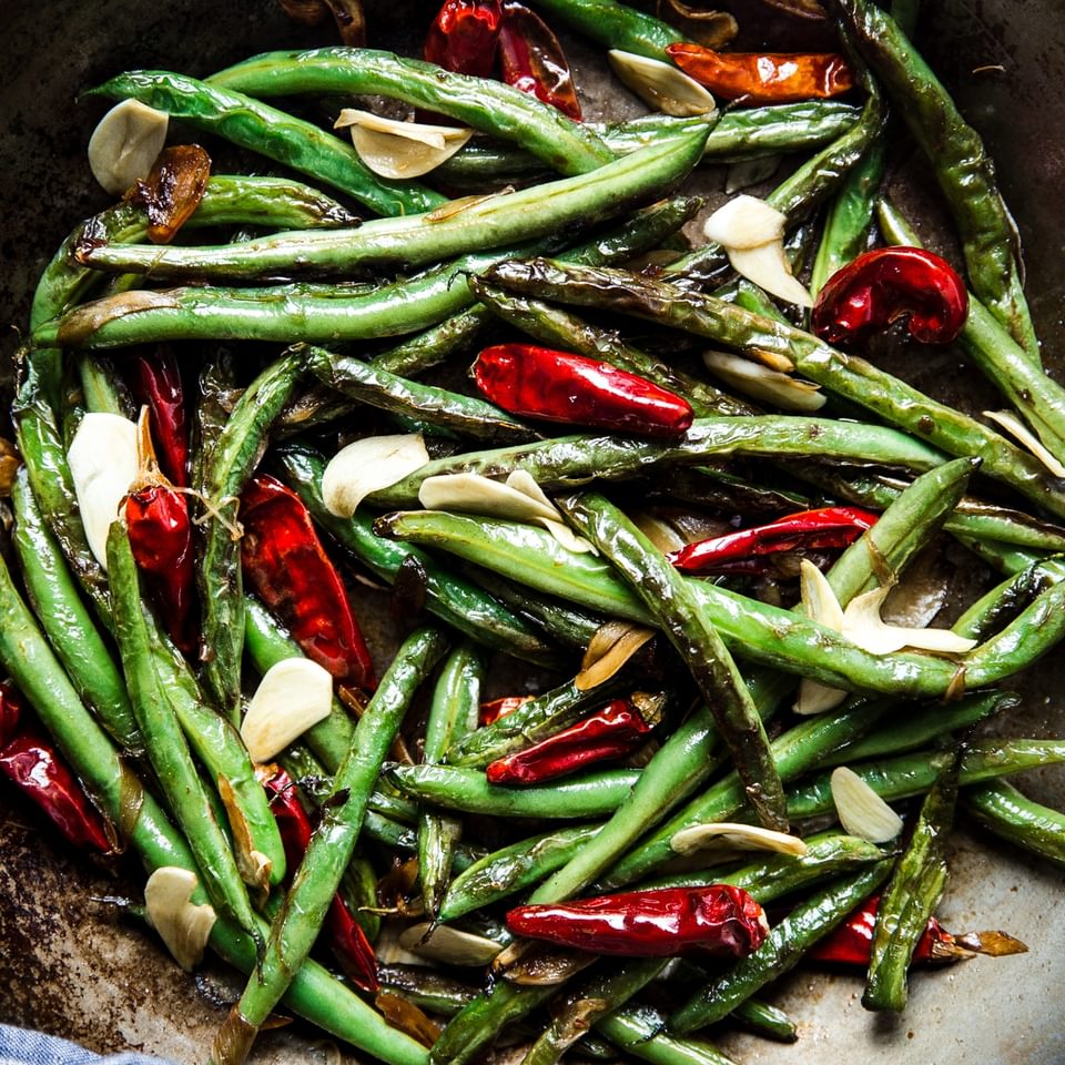 dry fried green beans in a skillet with red chillies and garlic cloves