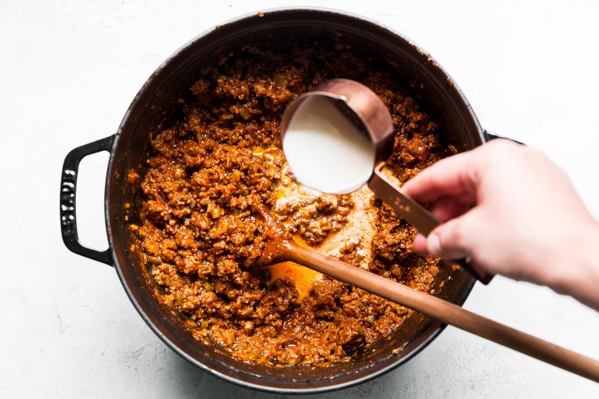 easy bolognese in a large pot with cream being added from a measuring cup