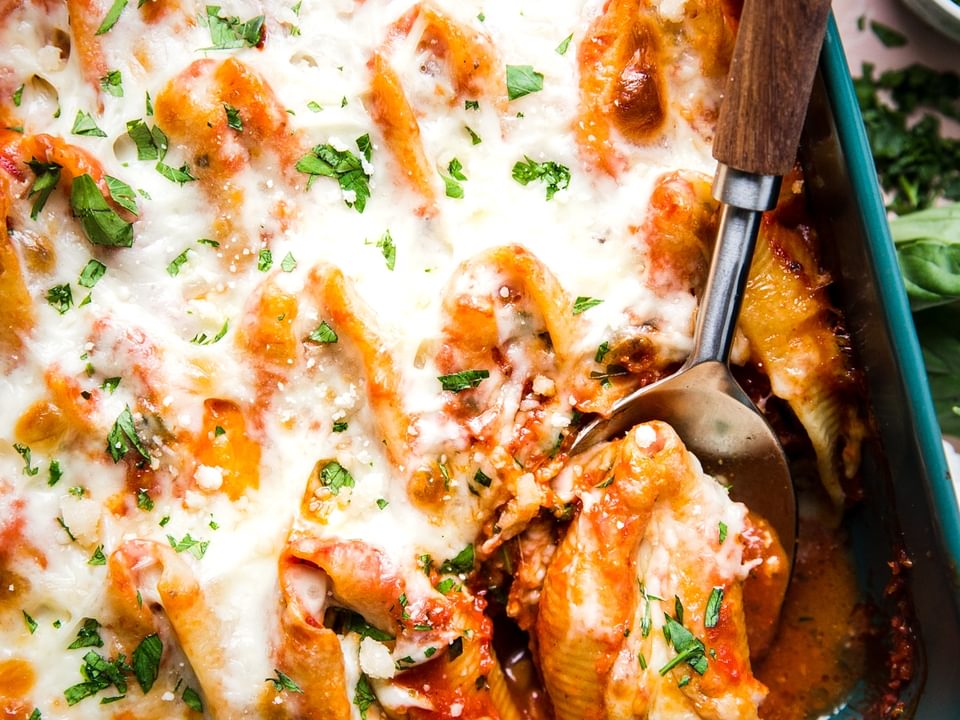 Easy Stuffed Pasta Shells in a pan with tomato sauce and mozzarella with a serving spoon