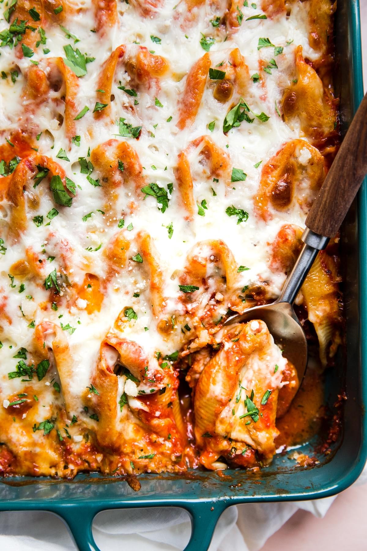 Easy Stuffed Pasta Shells in a pan with tomato sauce and mozzarella with a serving spoon