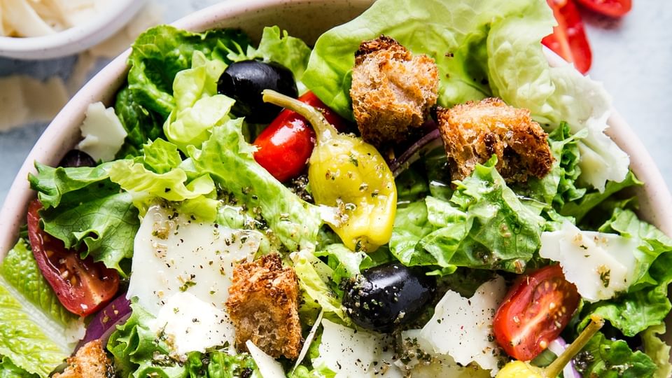 Italian Salad with romaine lettuce, croutons, tomatoes, pepperoncini, black olives, parmesan cheese and red onions in a bowl.