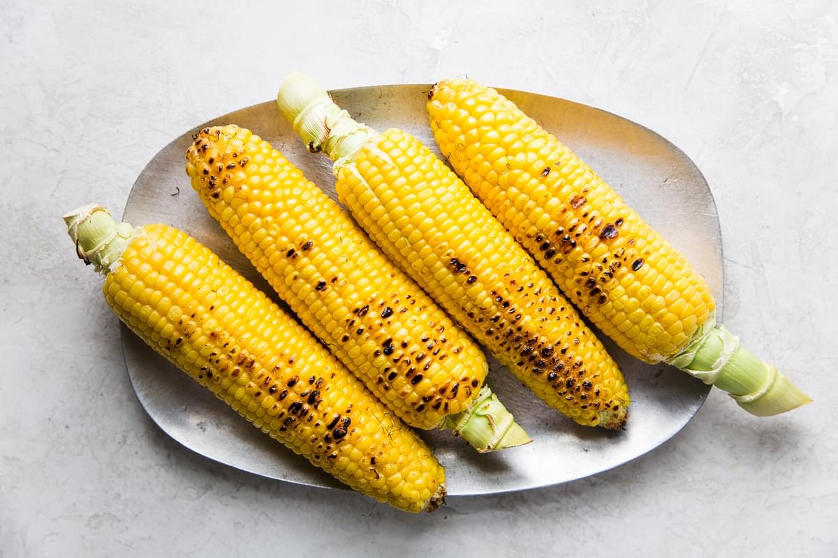 four grilled corn on the cob on a plate.