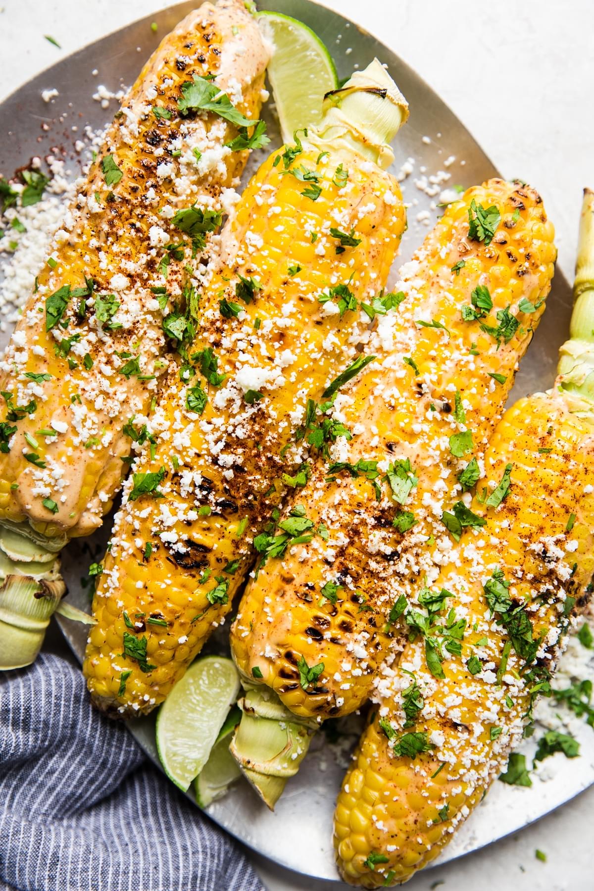 Plater of Elote (Mexican Street Corn) topped with fresh cilantro and slices of limes
