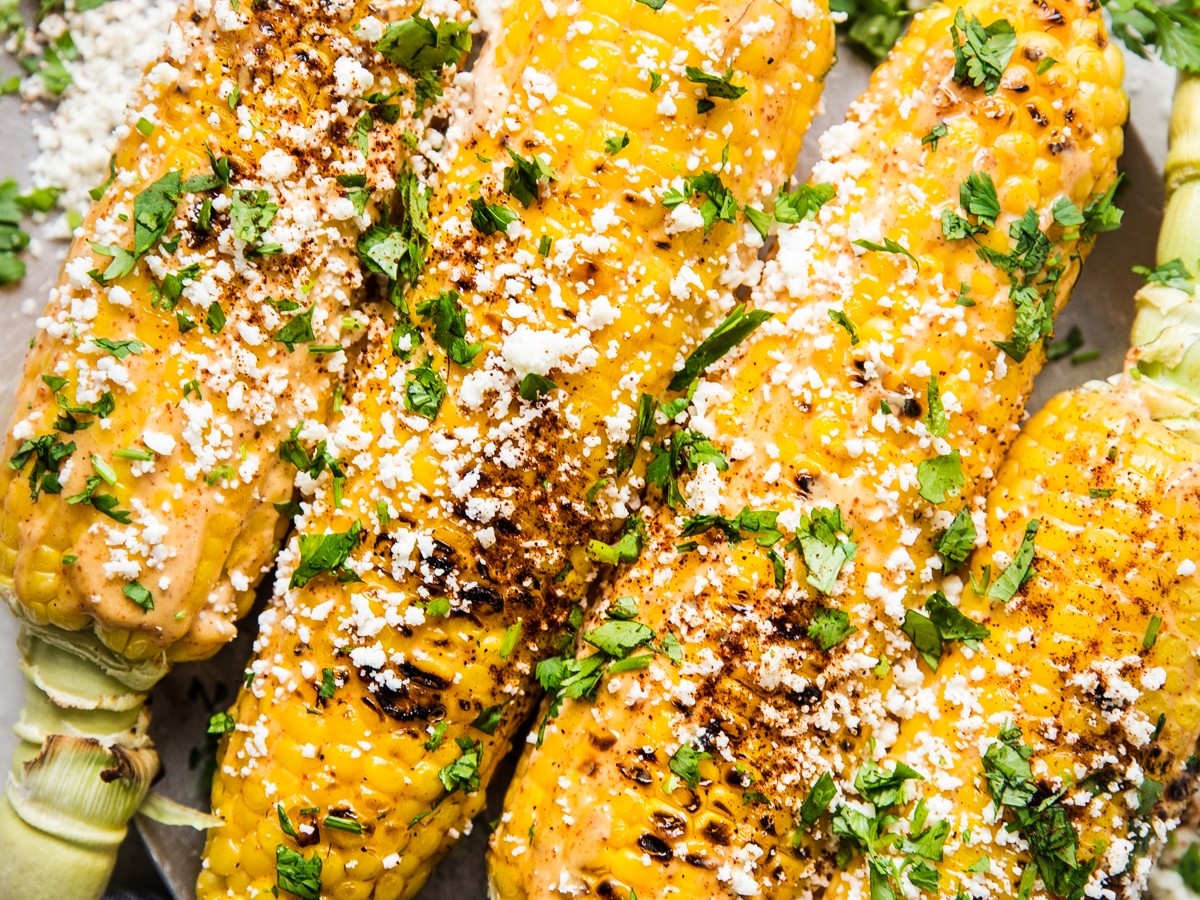 Plater of Elote Mexican Street Corn topped with fresh cilantro and slices of limes