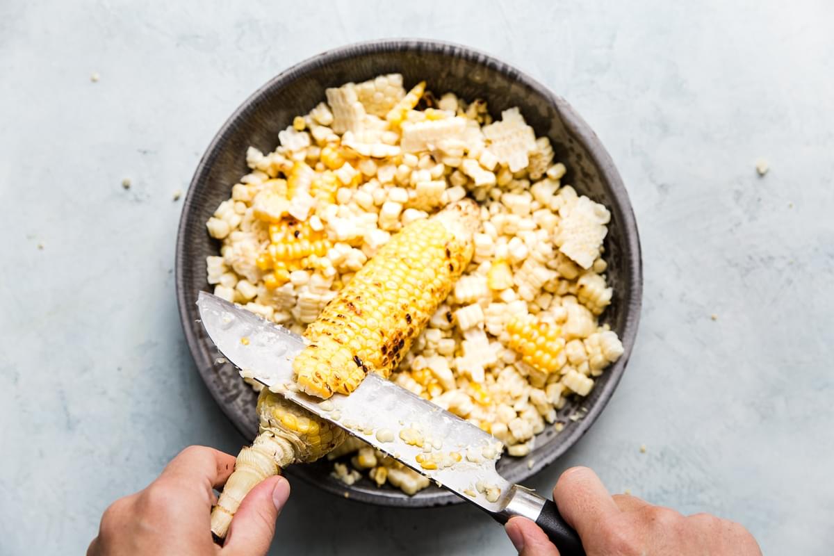 hand using sharp knife to remove corn kernels from corn ear