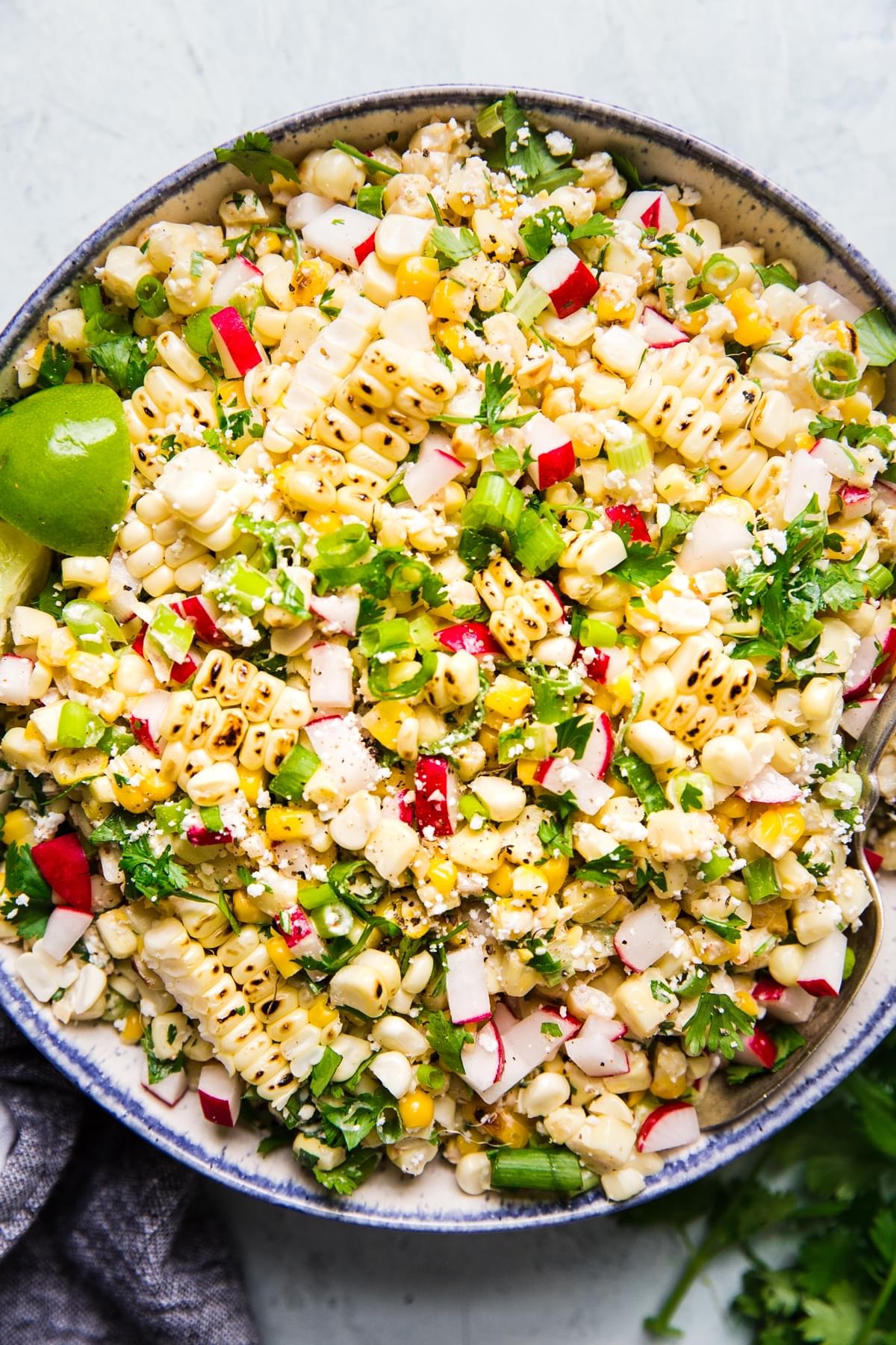 Mexican street corn salad in a large bowl with fresh lime wedges served on top