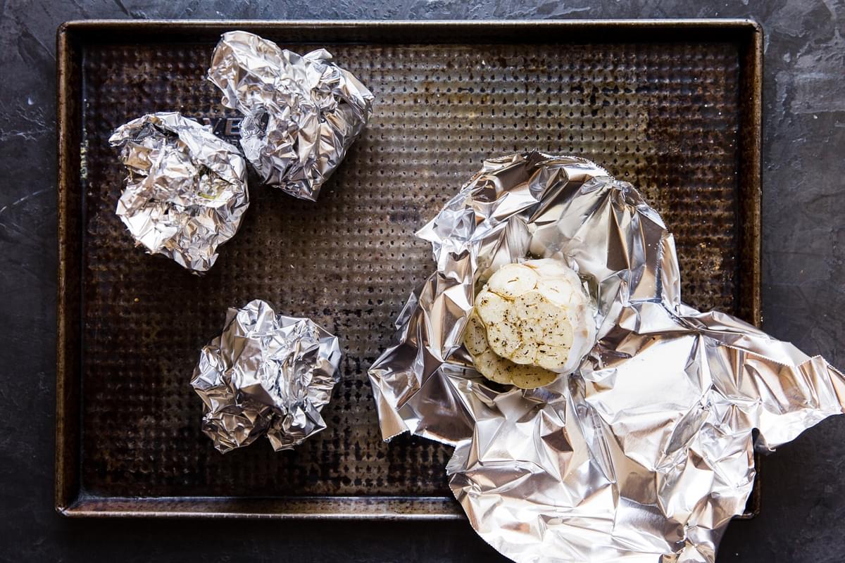raw garlic heads wrapped in foil with olive oil