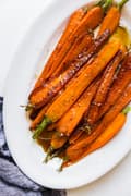 brown butter glazed orange carrots cut length wise on a white oval platter with a linen