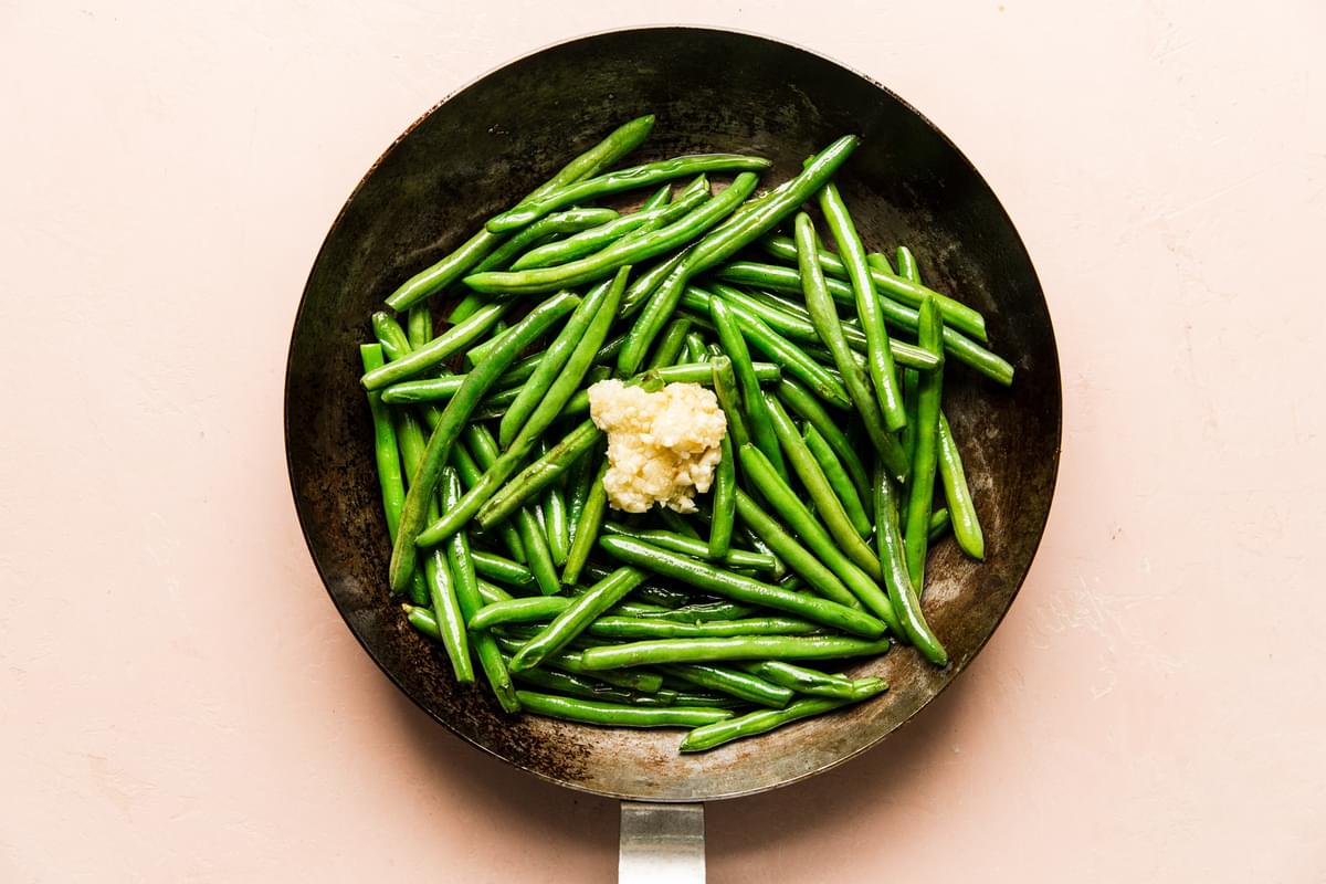 1 pound of fresh green beans cooking in a skillet with minced garlic.