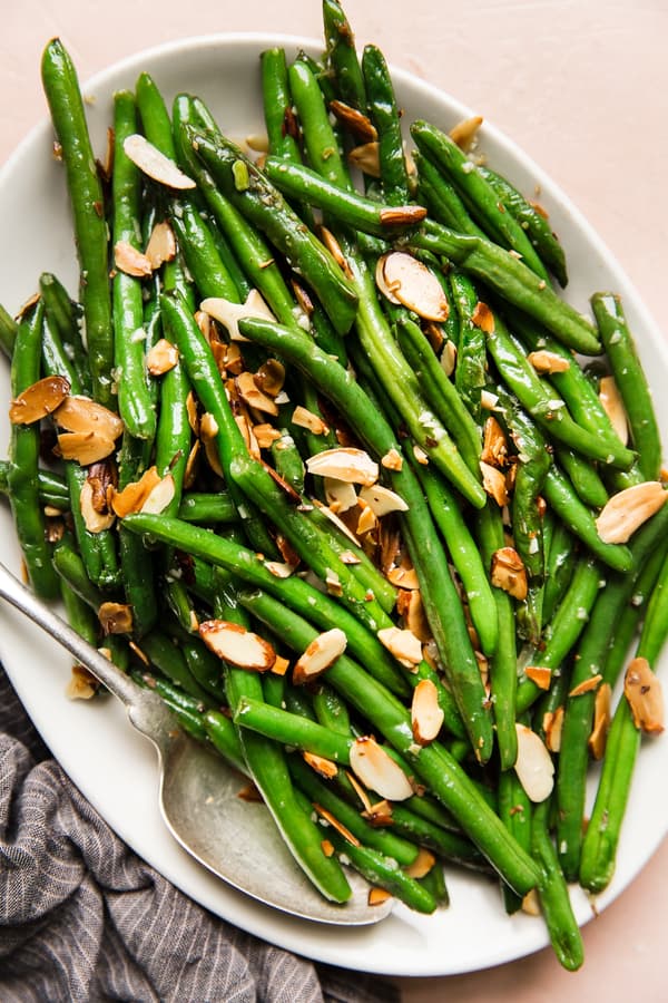green beans almondine with garlic and toasted almonds on a white platter with a spoon