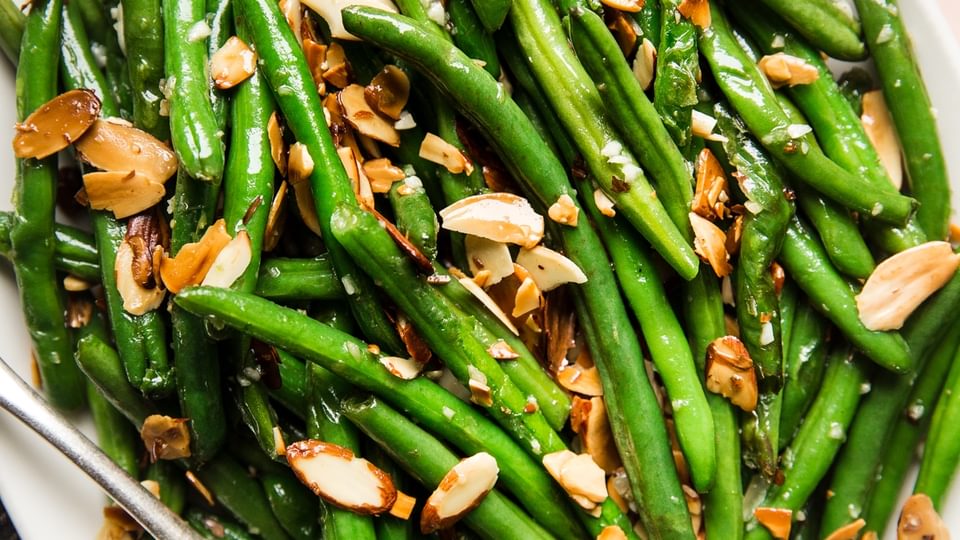 green bean almondine with garlic and toasted almonds on a white platter with a spoon