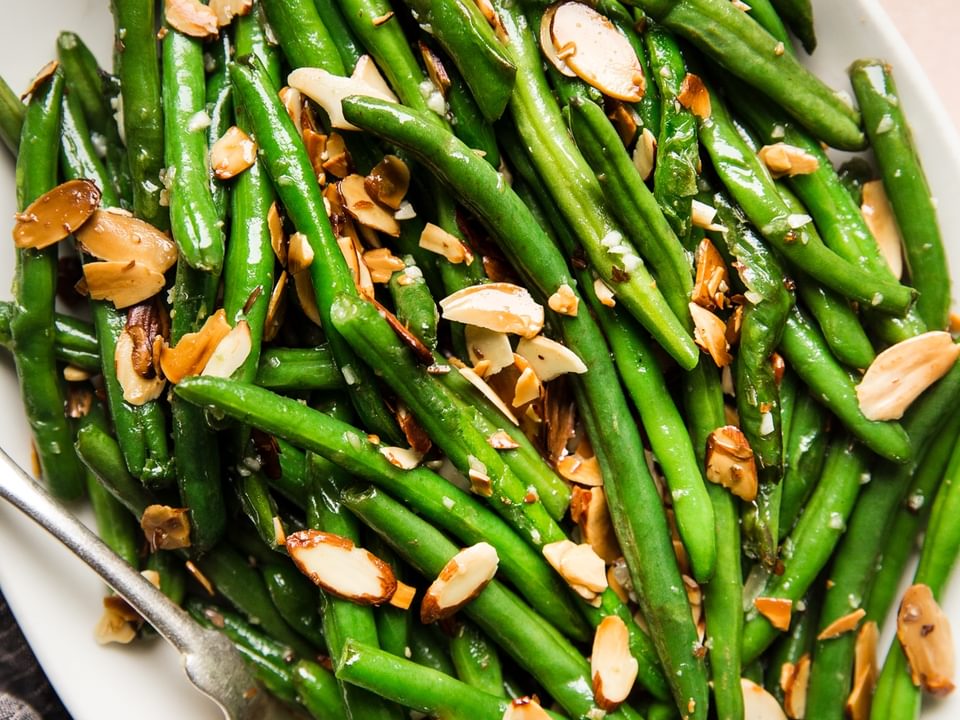 green bean almondine with garlic and toasted almonds on a white platter with a spoon