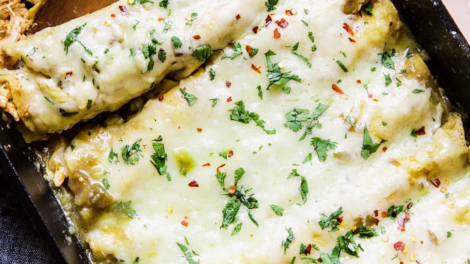 Cheesy Green Chicken Enchiladas in a pan with serving spoon