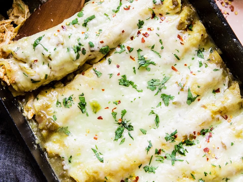 Cheesy Green Chicken Enchiladas in a pan with serving spoon