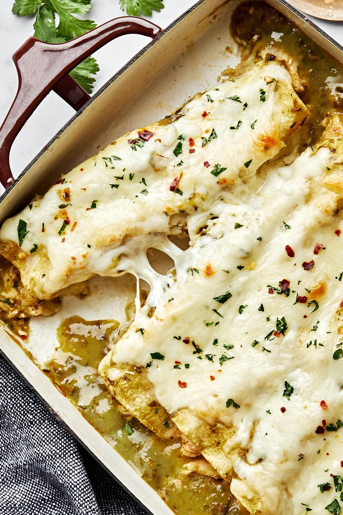 homemade green chicken enchiladas in a casserole dish made with chicken, cheese, sour cream and taco seasoning
