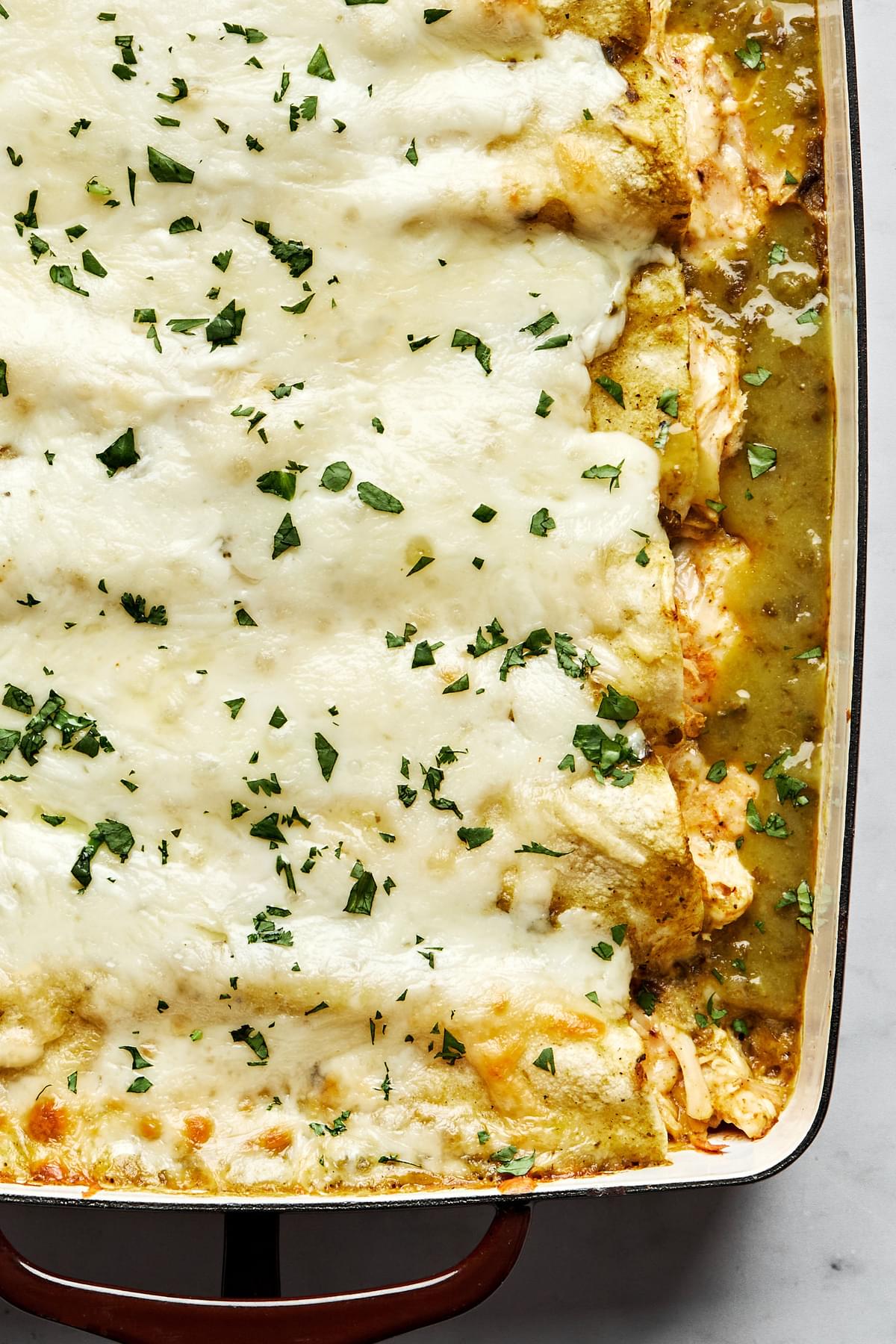 homemade green chicken enchiladas in a casserole dish made with chicken, cheese, sour cream and taco seasoning
