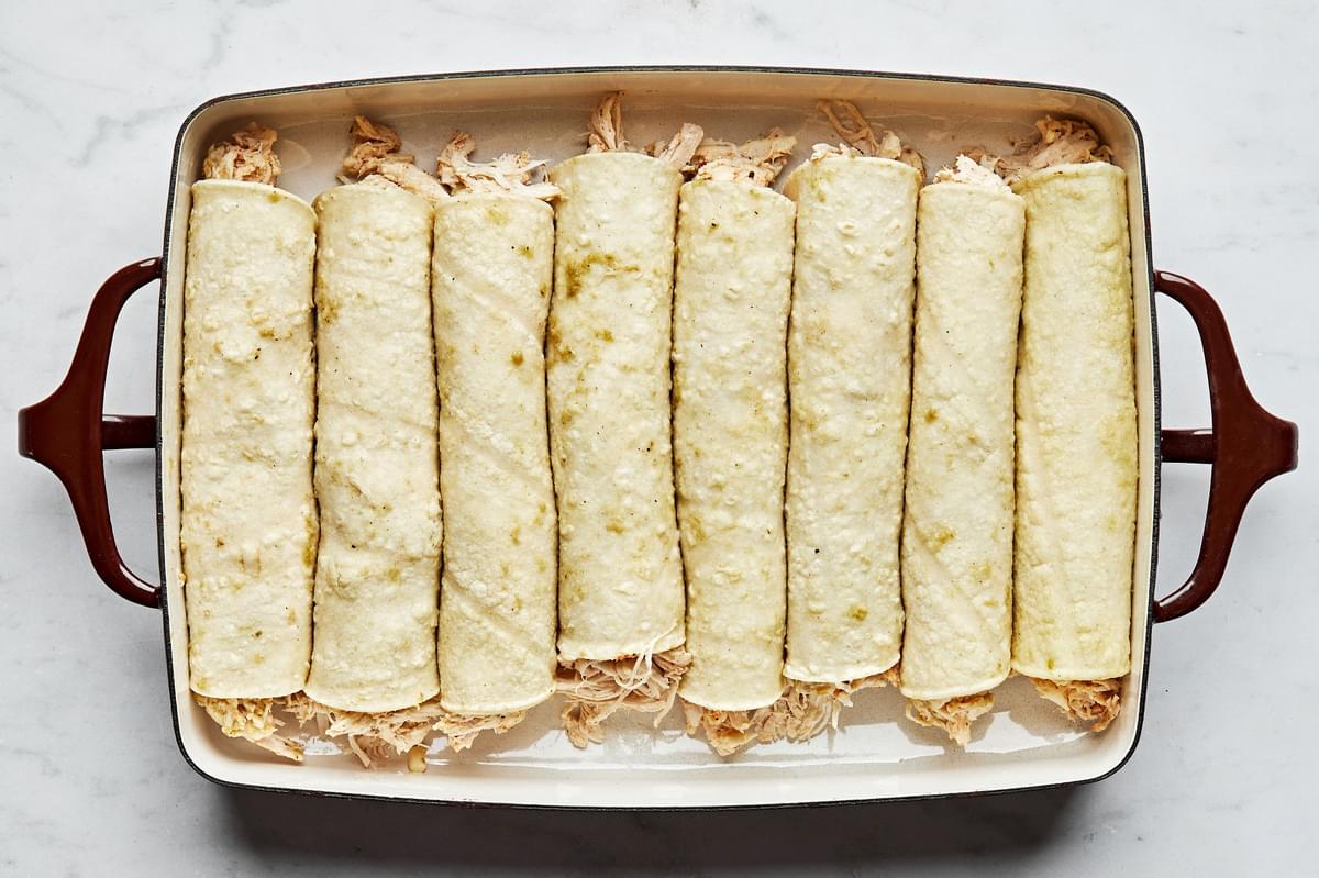 rolled green chicken enchiladas lined up in a casserole dish