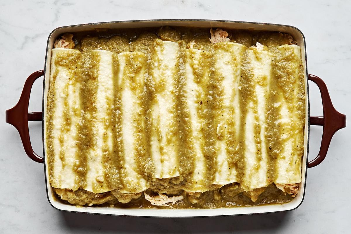rolled green chicken enchiladas lined up in a casserole dish topped with green enchilada sauce