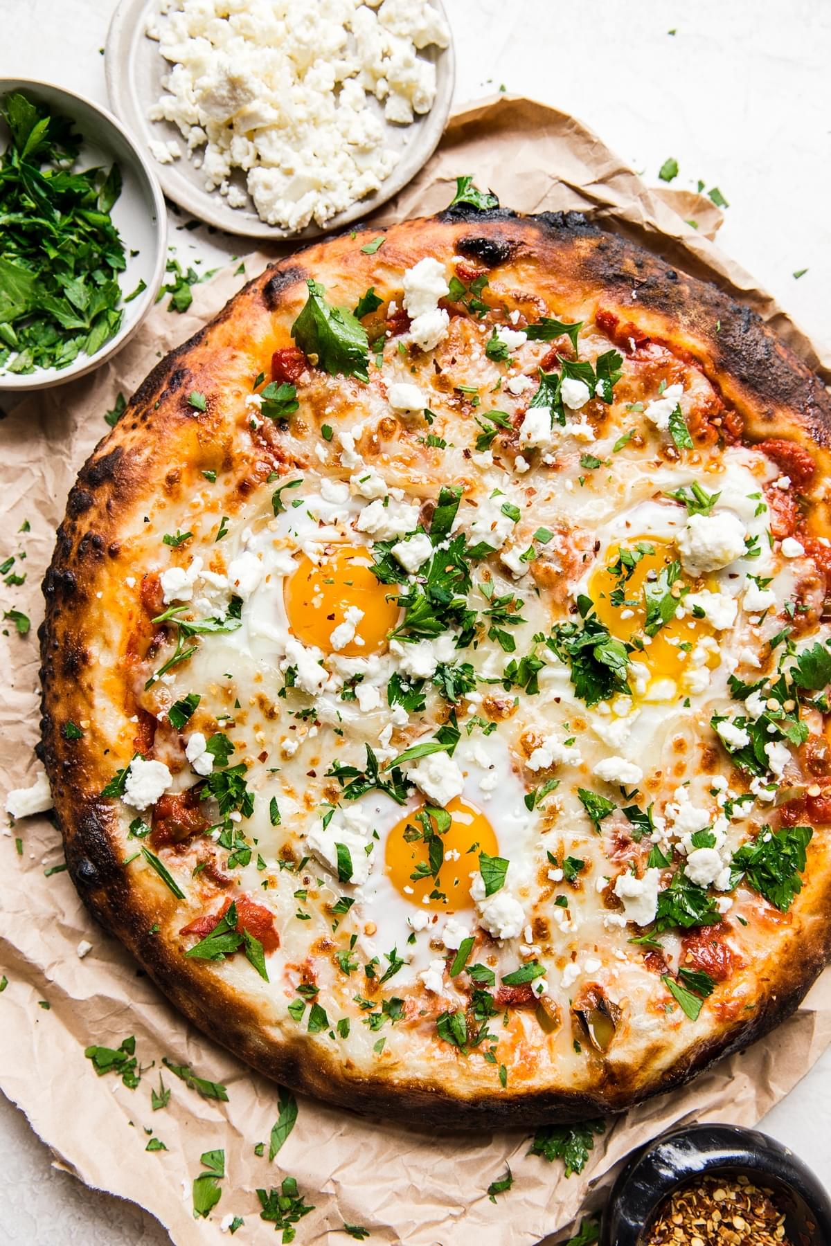 Whole grilled shakshuka pizza topped with feta and fresh parsley