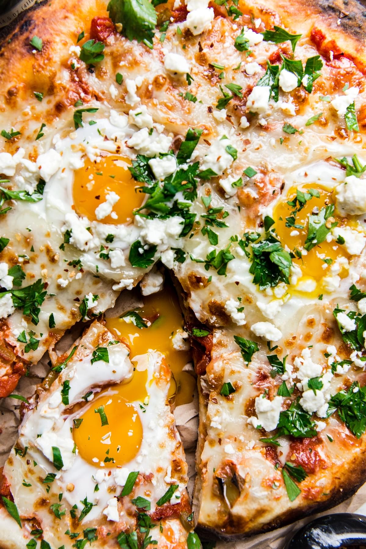 grilled shakshuka pizza with a slice cut out topped with eggs, feta and parsley