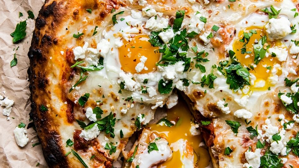 grilled shakshuka pizza with one slice out it and a side of finely chopped italian parsley