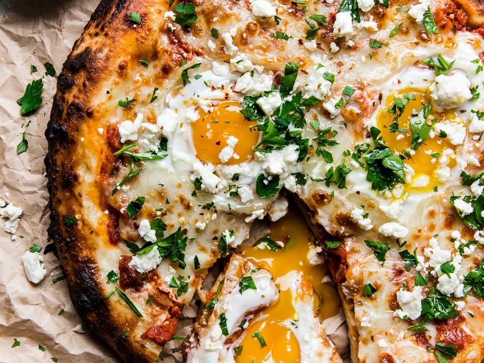 grilled shakshuka pizza with one slice out it and a side of finely chopped italian parsley