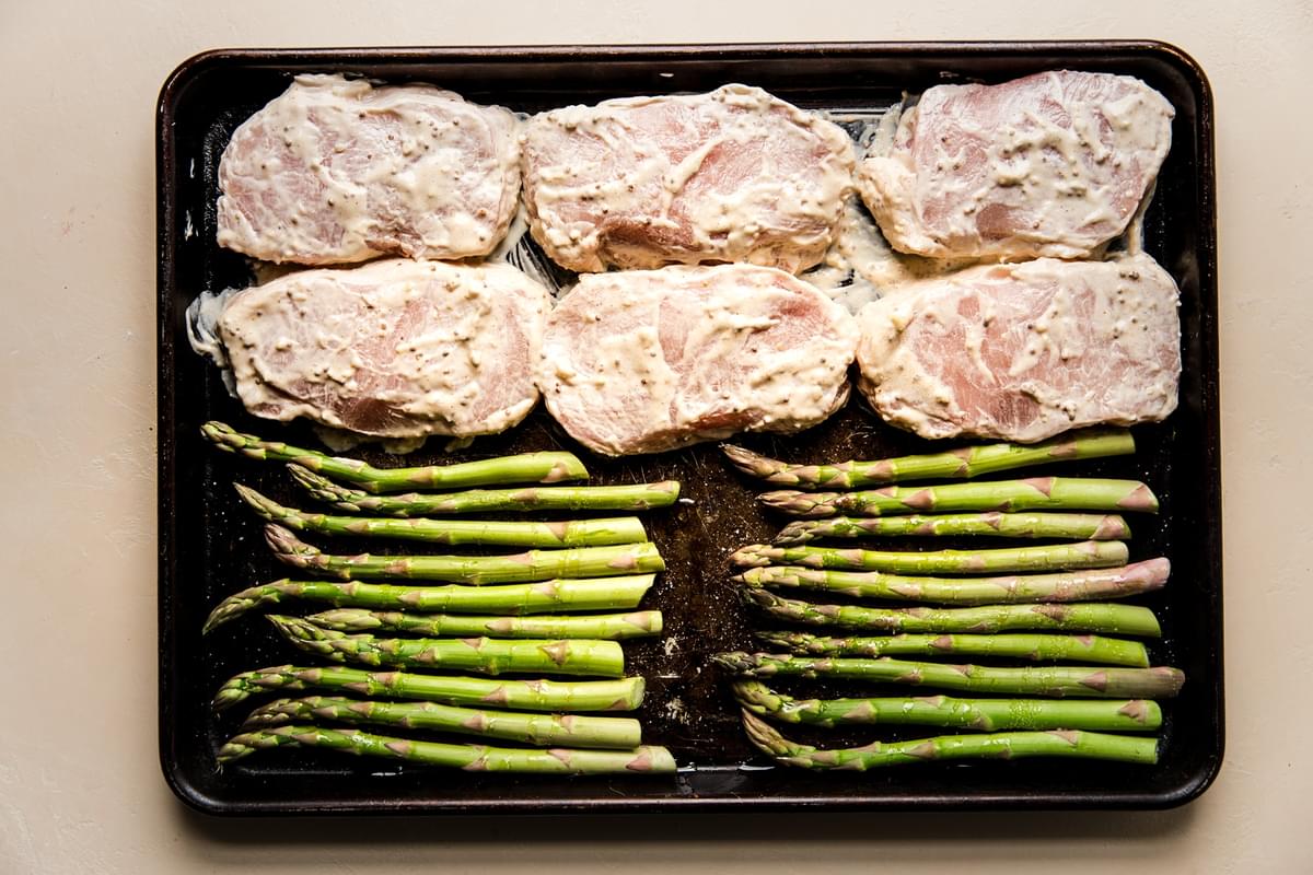 raw marinaded pork chops and asparagus on a sheet pan