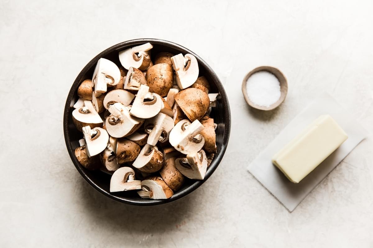 a bowl of quartered mushrooms in a bowl with salt and a stick of butter