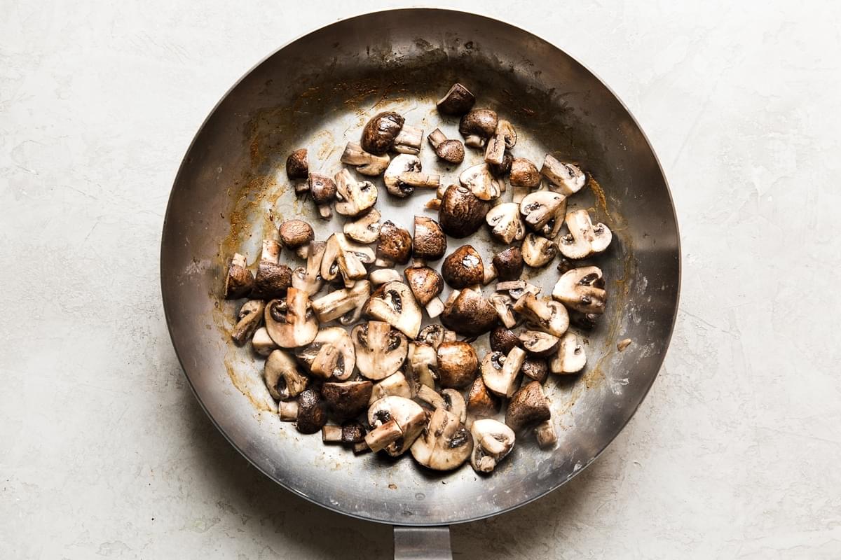 quartered brown crimini mushrooms cooking in a pan