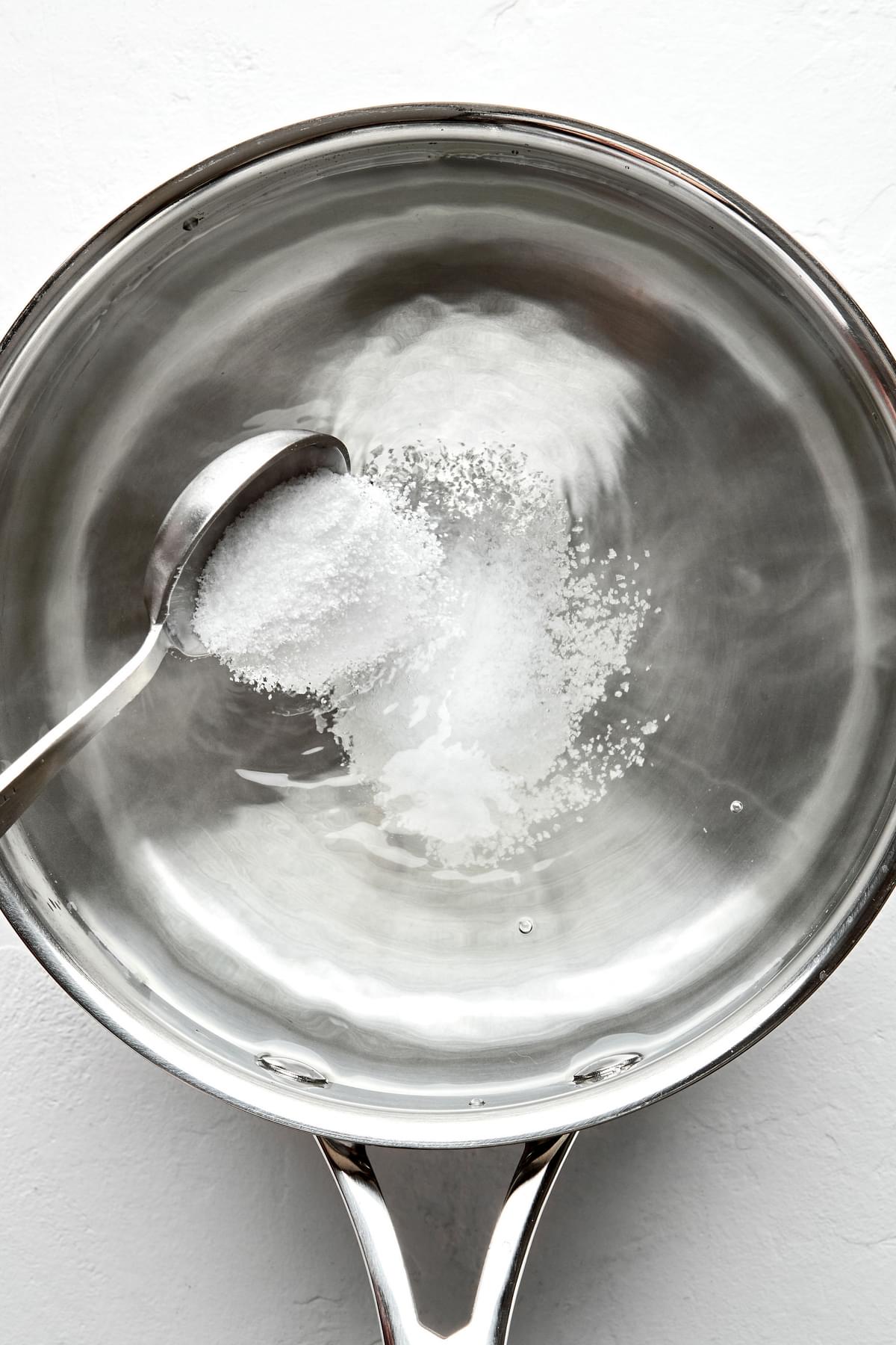 one tablespoon of salt being poured into a pot filled with 4 quarts of water to use to cook pasta noodles