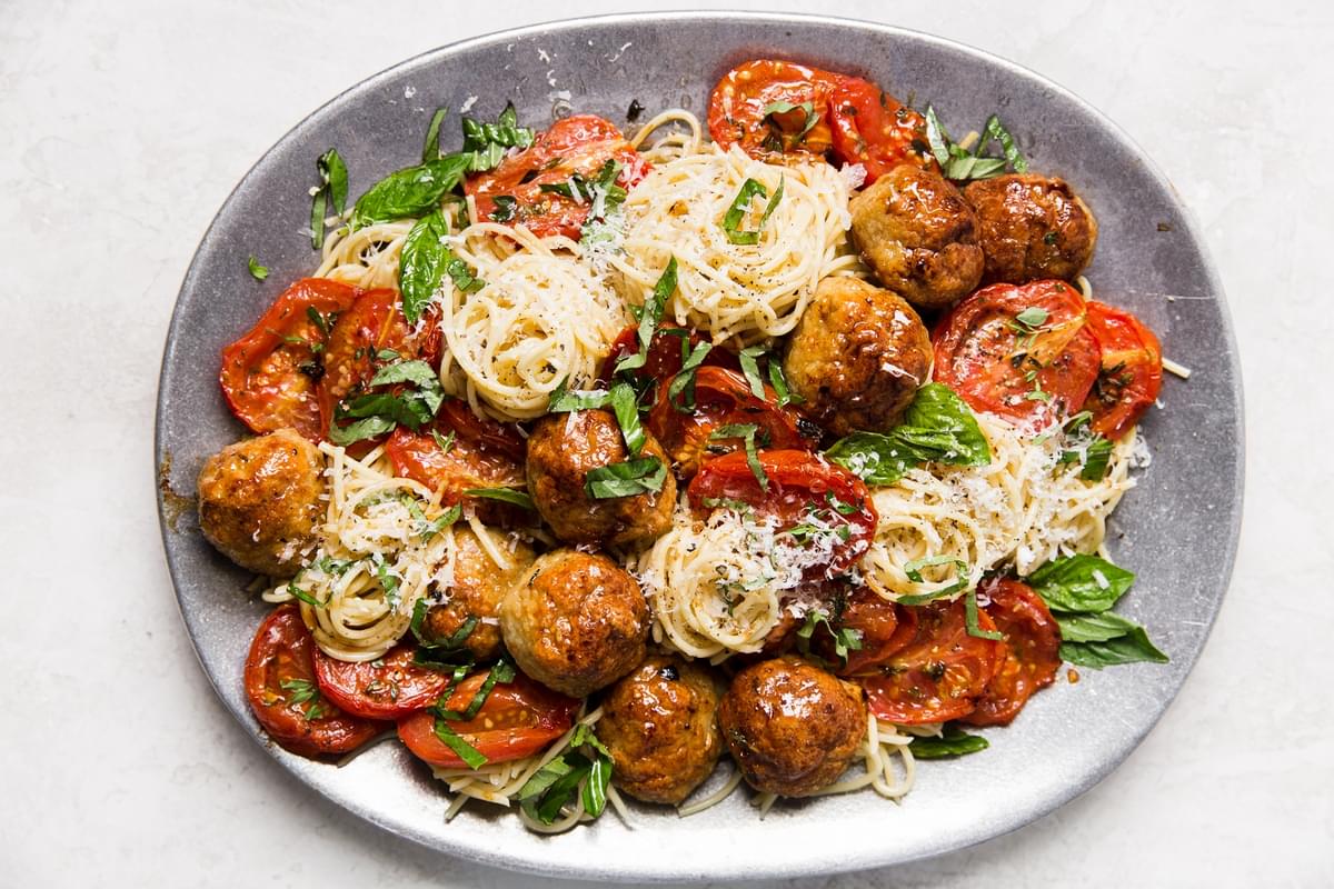 Italian chicken meatballs on a serving plate with spaghetti, basil, parmesan and roasted tomatoes.