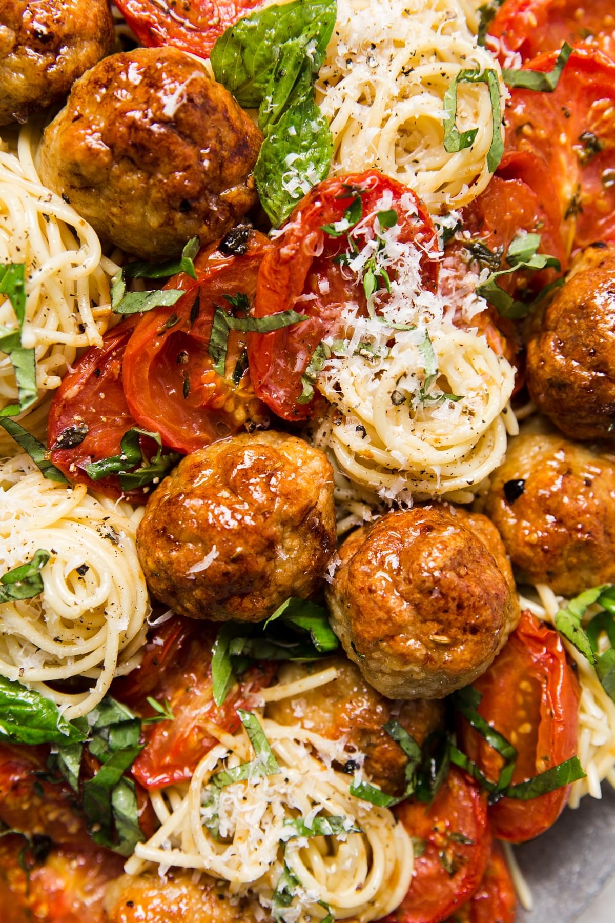 close up of Italian chicken meatballs with spaghetti, basil, parmesan and roasted tomatoes.