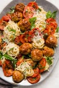 Italian Baked Chicken Meatballs on a platter with roasted tomatoes basil and pasta